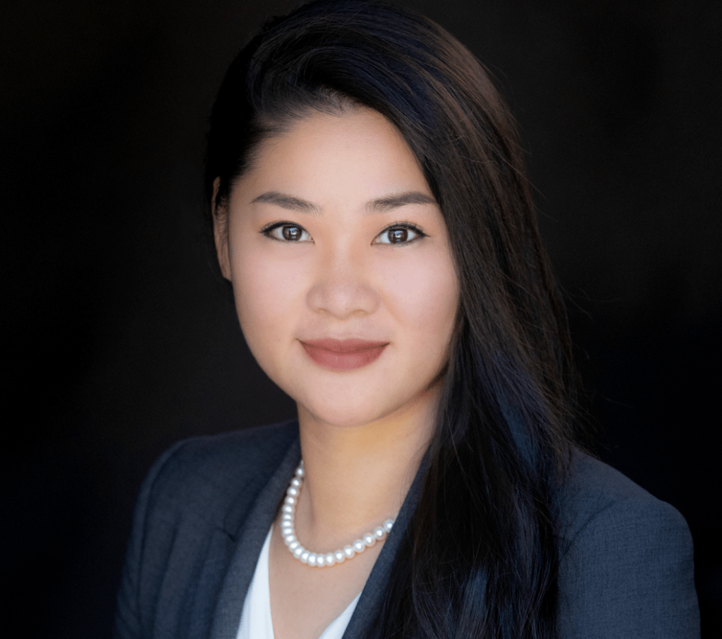 An Asian woman in a professional business suit, adorned with pearls, exudes confidence and elegance in a corporate setting.